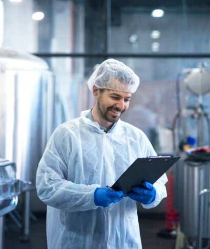 Industrial worker technologist in white suit with hairnet and protective gloves looking at checklist and smiling. Industrial worker technologist in white suit with hairnet and protective gloves looking at checklist and smiling.